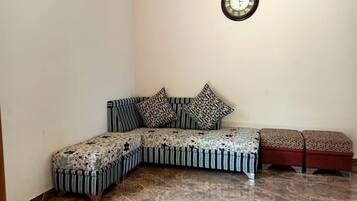 A corner room with a sofa, ottomans, a clock, and a tiled floor.