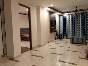 A spacious room with a tiled floor, a bed, a small table, and curtains.
