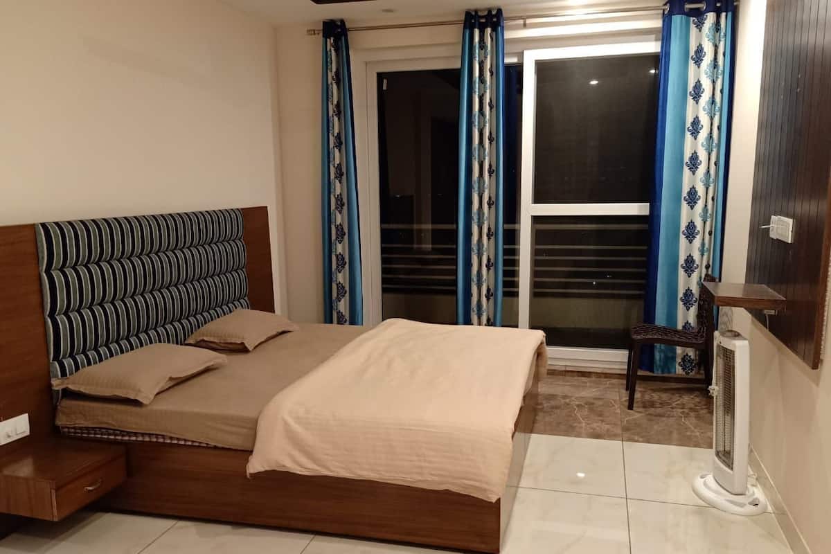 Un dormitorio con cama de madera, mesita de noche, una silla y una ventana con cortinas.