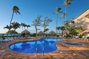 A pool area with lounge chairs and umbrellas, surrounded by palm trees and a view of the ocean.
