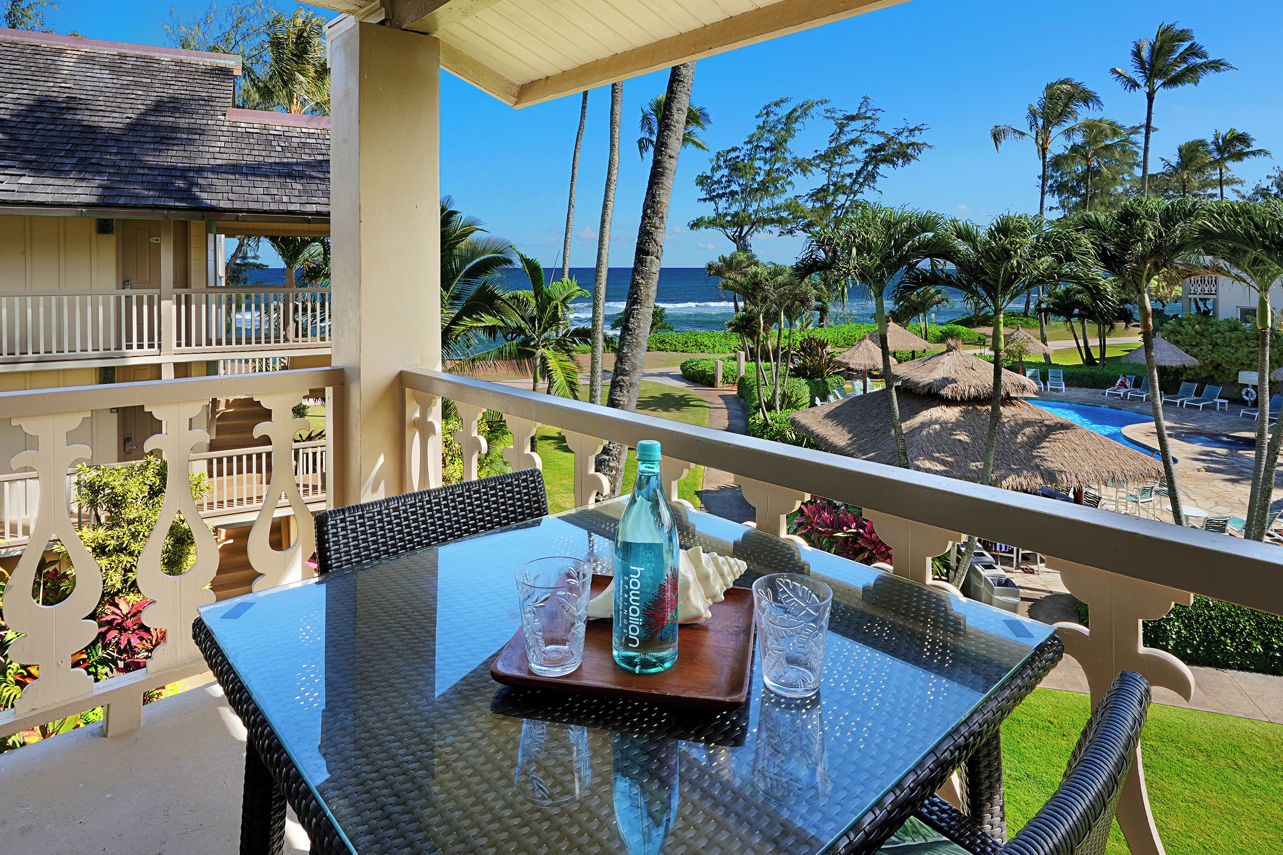 A balcony with a table, chairs, and a view of the ocean and palm trees.