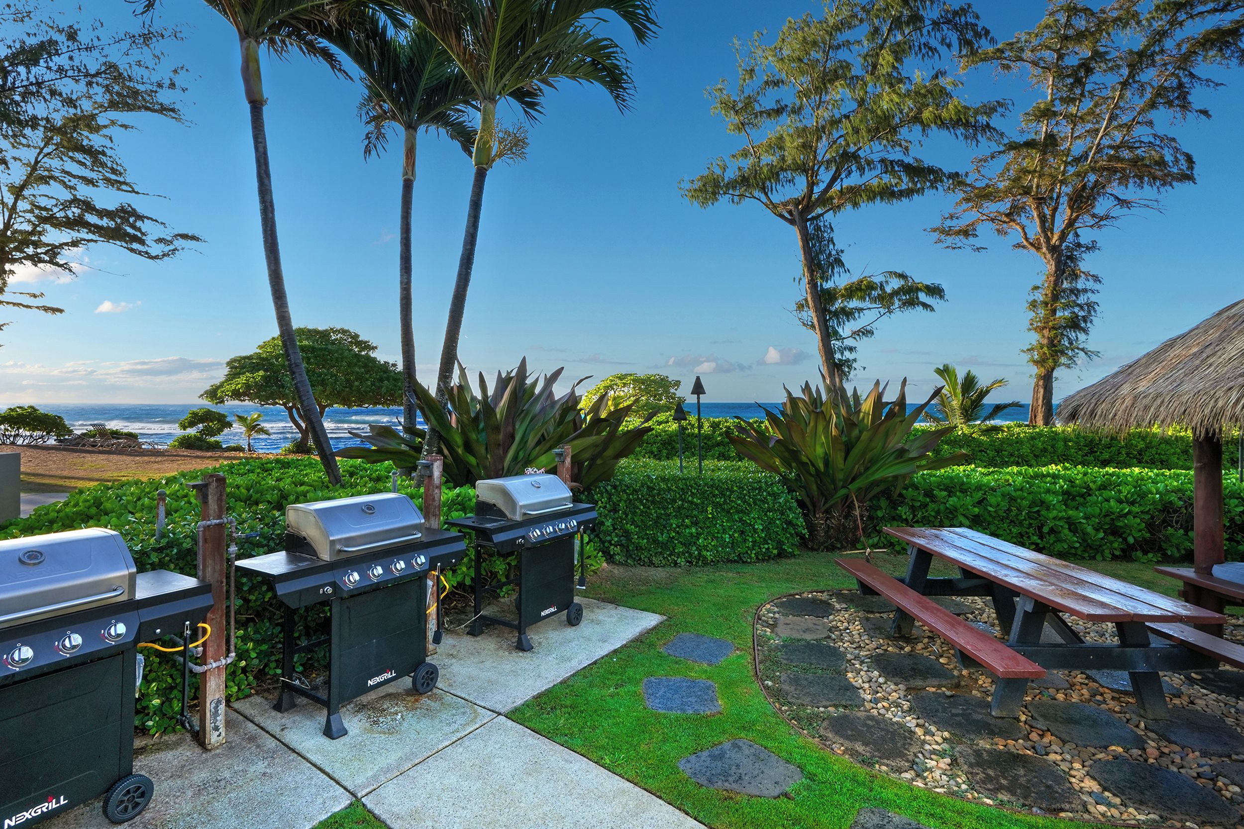 An outdoor grilling area with two grills, a picnic table, and a view of the ocean.