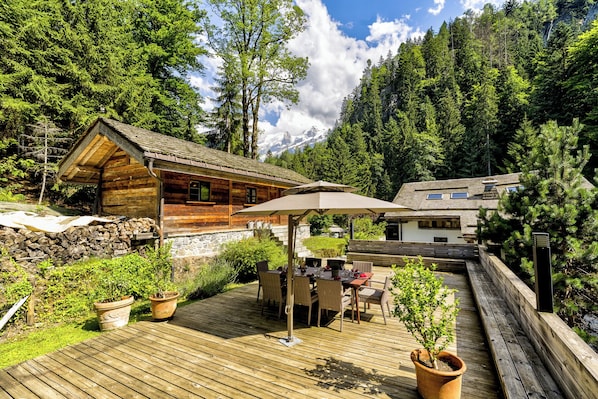 A wooden cabin with a deck, outdoor seating, and a mountain backdrop.
