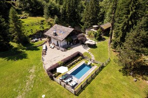 Una casa con piscina, rodeada por una terraza de madera y un muro de piedra.