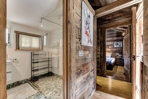 Un interior rústico con paredes de madera, baño con suelo de piedra, cama con cabecero de madera y una obra de arte enmarcada en la pared.