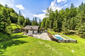 Un chalet avec piscine, entouré de forêt.