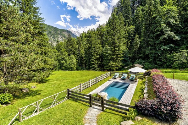 Un espace piscine avec des chaises longues, une terrasse en bois et une vue sur une chaîne de montagnes boisées.