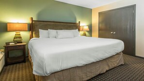 A hotel room with a large bed, two bedside lamps, a wooden nightstand, a door, and a patterned carpet. - Wisconsin Dells Cottage Escape with Golf, Pools & Spacious 2BR Family Stay (Wisconsin Dells)