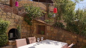 Un área de comedor al aire libre con pared de piedra, una mesa con sillas y luces rojas colgantes.
