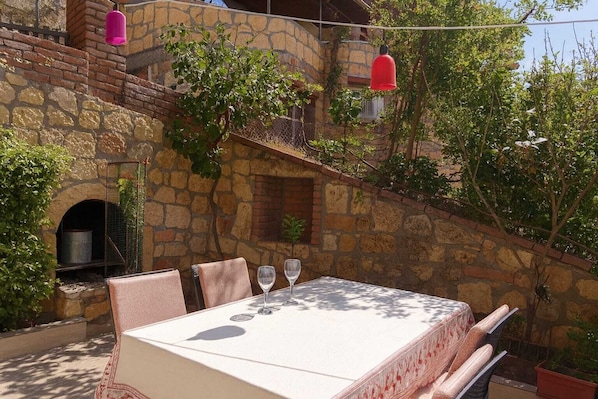An outdoor dining area with a stone wall, a table with chairs, and hanging red lights.