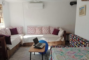 A room with two beds, a laptop on a small table, and a colorful blanket on the floor.