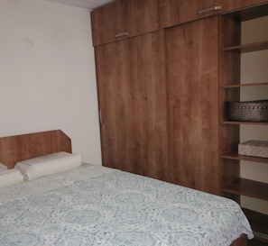 A bedroom with a bed, a wooden wardrobe, and a shelf unit.