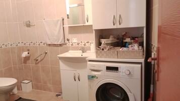 A bathroom with a toilet, sink, washing machine, and a mirror.