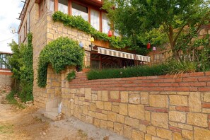 A stone building with a brick wall, a covered outdoor seating area, and greenery.
