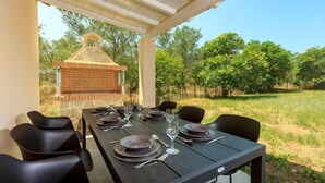 A covered outdoor dining area with a brick barbecue, black dining chairs, and a table set for four. - Mary's Country House (Lefkimmi)