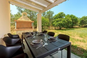 A covered outdoor dining area with a brick barbecue, black dining chairs, and a table set for four. - Mary's Country House (Lefkimmi)