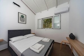 A modern bedroom with a bed, bedside tables, a window with a view, and a wall-mounted air conditioner. - Mary's Country House (Lefkimmi)