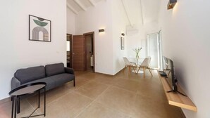 A modern living room with a sofa, a small table, a dining area with chairs, and a TV on a stand. - Mary's Country House (Lefkimmi)