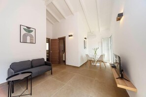 A modern living room with a sofa, a small table, a dining area with chairs, and a TV on a stand. - Mary's Country House (Lefkimmi)