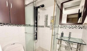 Bany amb plat de dutxa de vidre, un lavabo de vidre i un salvasalls de rajola.