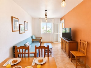 Una sala de estar acogedora con sofá, mesa de comedor, sillas, televisor y ventana con cortinas.
