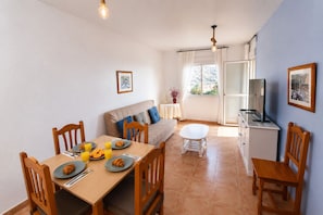 A dining area with a table set for breakfast, a sofa, a TV, and a window with curtains.