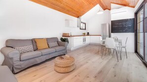 A modern living space with a wooden ceiling, a grey sofa, a dining table with chairs, and a kitchen area. - Una Casa Canaria Moderna (Ingenio)