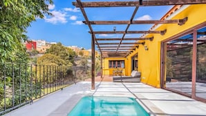 Uma área ao lado da piscina com pérgola, sofá e mesa.
