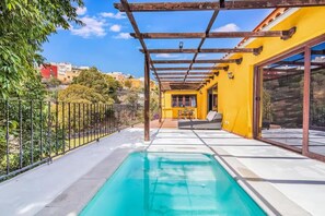 A poolside area with a pergola, a sofa, and a table.