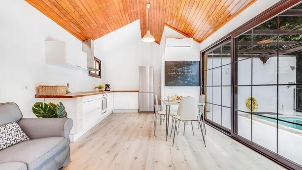 A modern kitchen with white cabinets, a wooden ceiling, and a dining area with white chairs. - Una Casa Canaria Moderna (Ingenio)