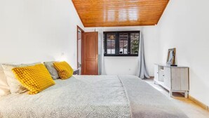 A bedroom with a bed, a wooden ceiling, a window, and a bedside table. - Una Casa Canaria Moderna (Ingenio)