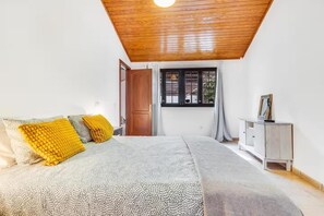 Een slaapkamer met een bed, houten plafond, een raam en een nachtkastje.