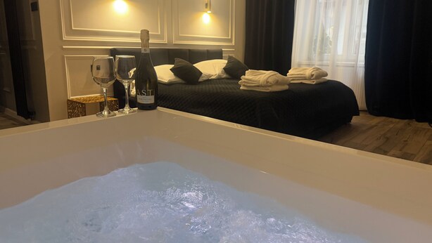 A hotel room with a bathtub filled with water, a bed with pillows, a bottle of wine, and two glasses on a side table. - Apartament z Jacuzzi Kraków SHINE Starowiślna (Kraków)