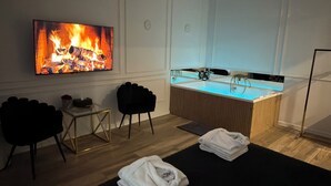 A room with a TV displaying a fire, a sink, two chairs, and towels on the floor. - Apartament z Jacuzzi Kraków SHINE Starowiślna (Kraków)