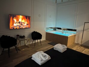 Una habitación con televisión mostrando un fuego, un lavamanos, dos sillas y toallas en el suelo.