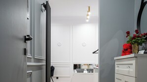 A hallway with a wooden floor, white walls, a black radiator, and a white cabinet with a vase of red flowers. - Apartament z Jacuzzi Kraków SHINE Starowiślna (Kraków)