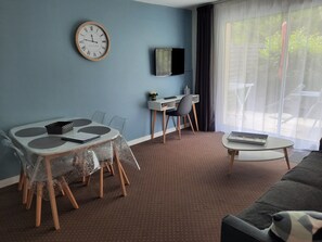 A hotel room with a dining table, chairs, a sofa, a TV, and a large window. - Apartment AB du parc of 51 M2 sunny - with beautiful terrace of 15M2 (Neufchâtel-Hardelot)