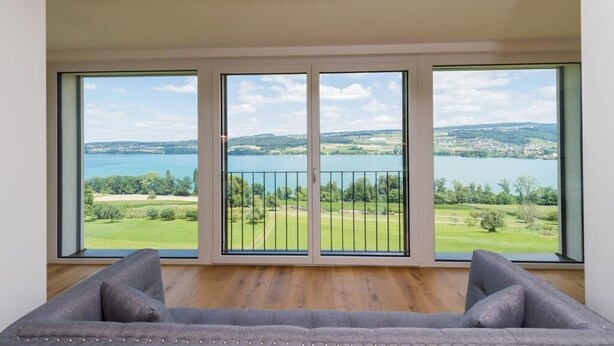 A room with a large window overlooking a lake and greenery.