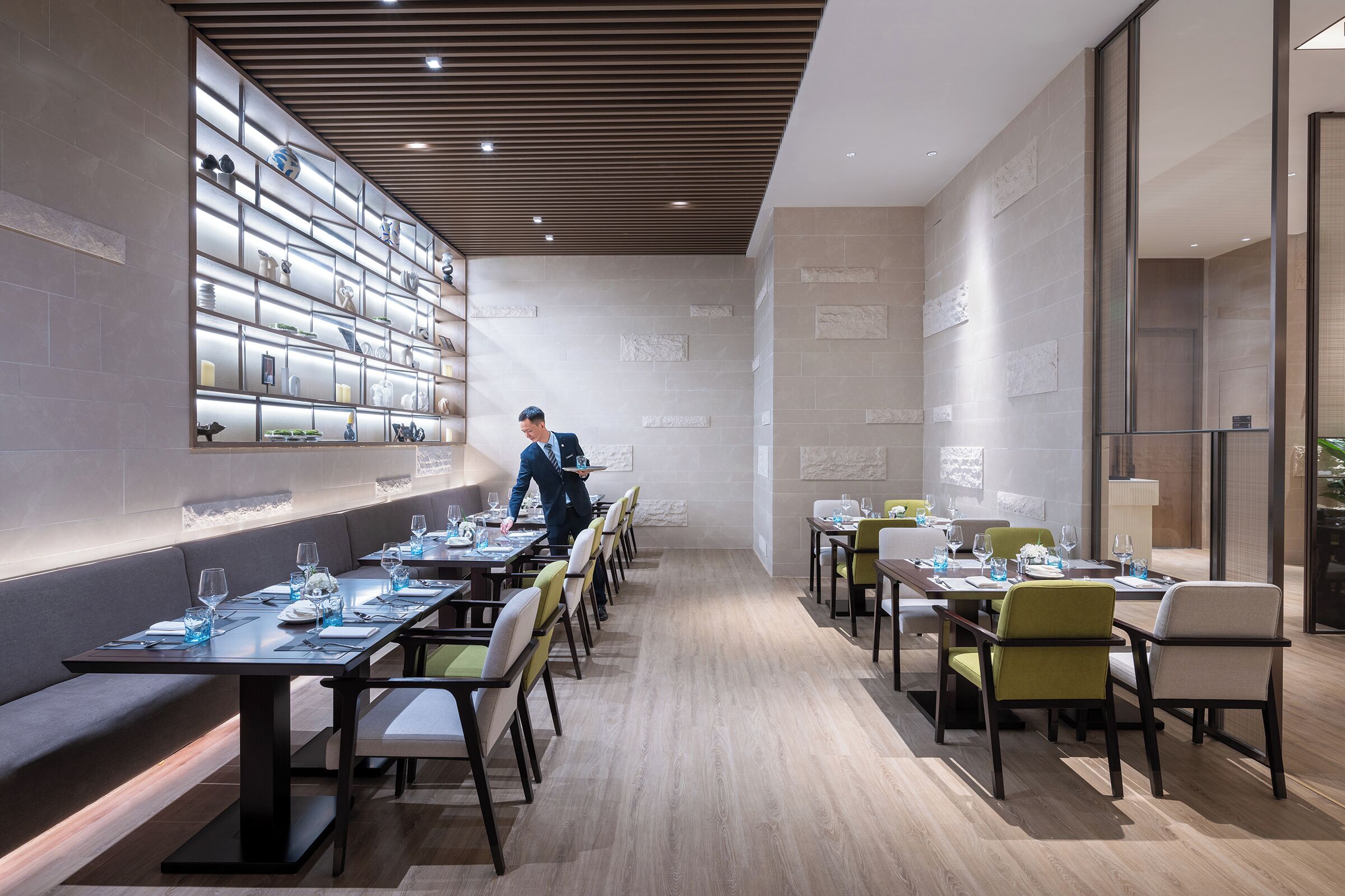 Un comedor moderno con mesas largas, sillas y una pared que exhibe diversos objetos.
