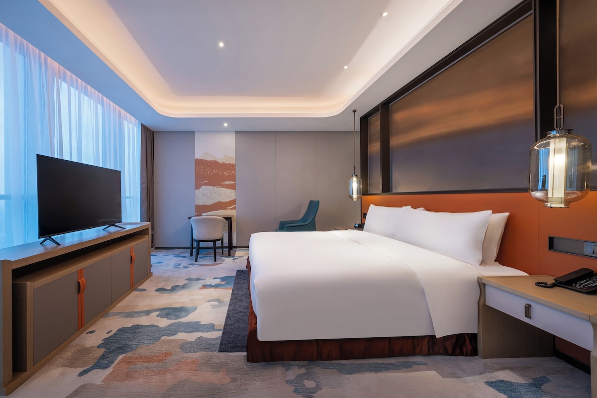 A hotel room with a bed, a TV, a desk, a chair, and a lamp.