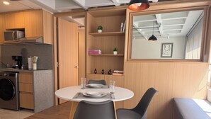 Una cucina compatta con elettrodomestici moderni, un'area pranzo con due sedie, una panca e una piccola libreria con libri e una pianta.