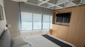 Una camera da letto con un letto, una sedia, una TV a muro e una finestra con tende.