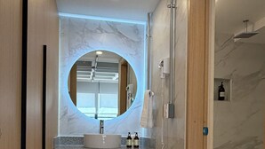 Un bagno moderno con uno specchio rotondo, mobili in legno, un lavandino e una zona doccia.