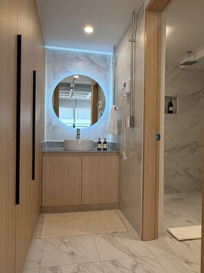 Ein modernes Badezimmer mit einem runden Spiegel, Holzschränken, einem Waschbecken und einer Duschkabine.