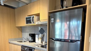 Eine kleine Küche mit Edelstahl-Kühlschrank, Waschmaschine, Mikrowelle und Kaffeemaschine.