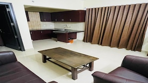 A living room with a sofa set, a coffee table, and a kitchen area with cabinets and a sink. - Tyche Stays (Thiruvananthapuram)