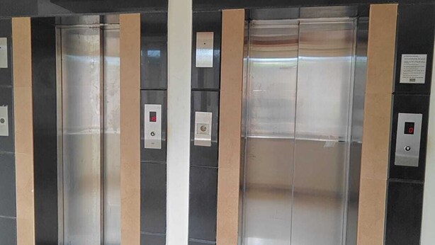 Four elevator doors with control panels, a tiled floor, and a wooden ceiling. - Tyche Stays (Thiruvananthapuram)
