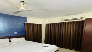 A hotel room with a bed, a ceiling fan, an air conditioning unit, and curtains. - Tyche Stays (Thiruvananthapuram)