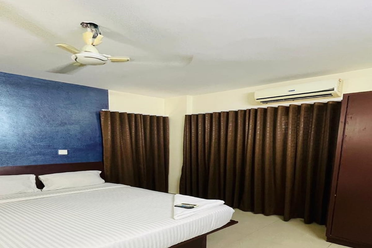 A hotel room with a bed, a ceiling fan, an air conditioning unit, and curtains.