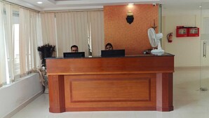 A reception desk with two individuals behind it, a wall-mounted fan, and a fire extinguisher on the wall. - Tyche Stays (Thiruvananthapuram)